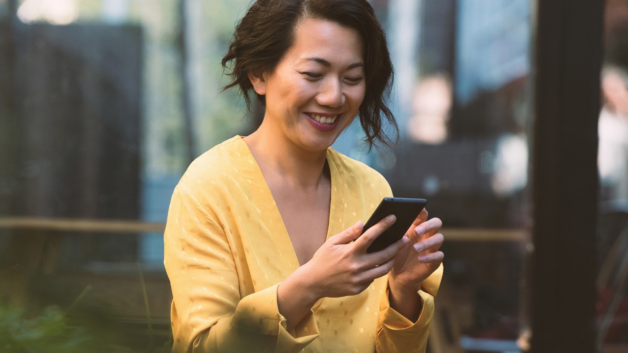 一個女人愉快地看著她的手提電話; 圖片應用於滙豐澳門多樣化理財方法頁面。